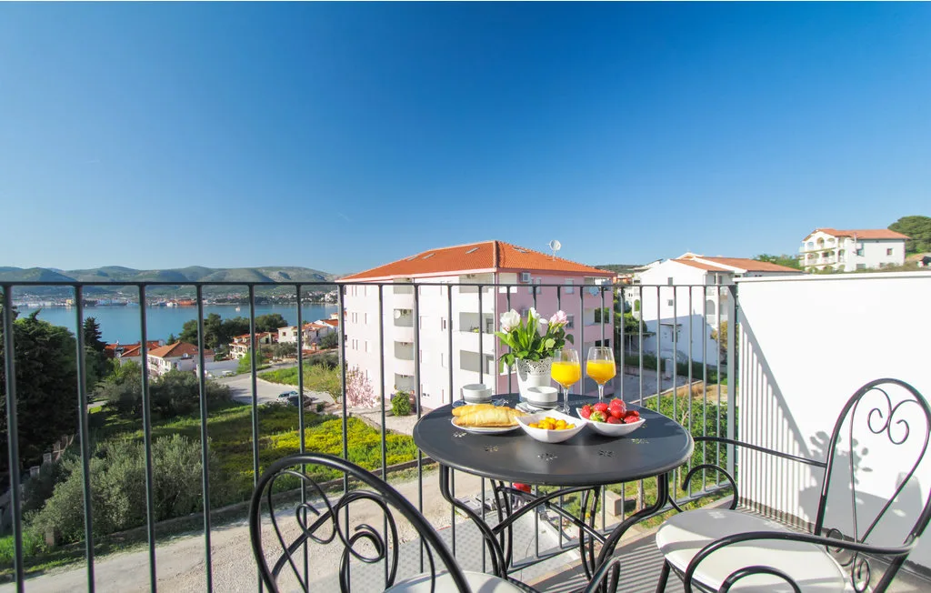 Una zona de comedor en un balcón ofrece vistas de edificios cercanos y una bahía costera.