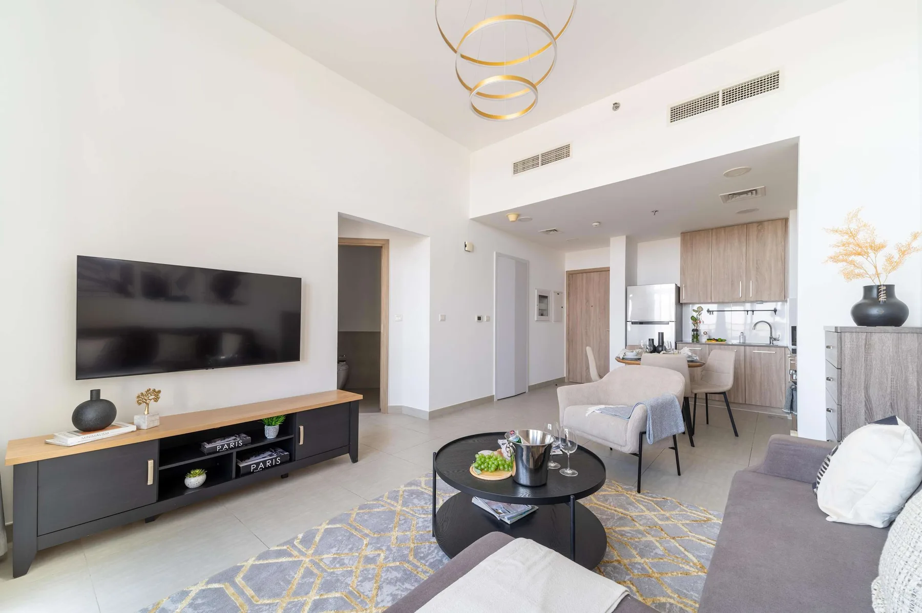 A bright living room with a television, seating, and an open kitchen area.