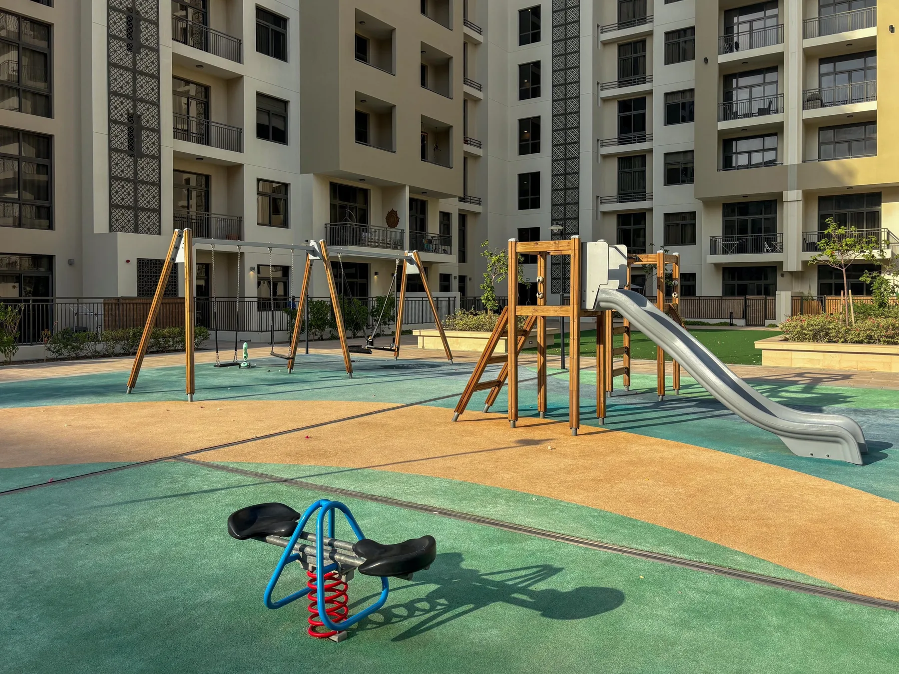 Un parque infantil al aire libre con tobogán y columpios junto a edificios de apartamentos.