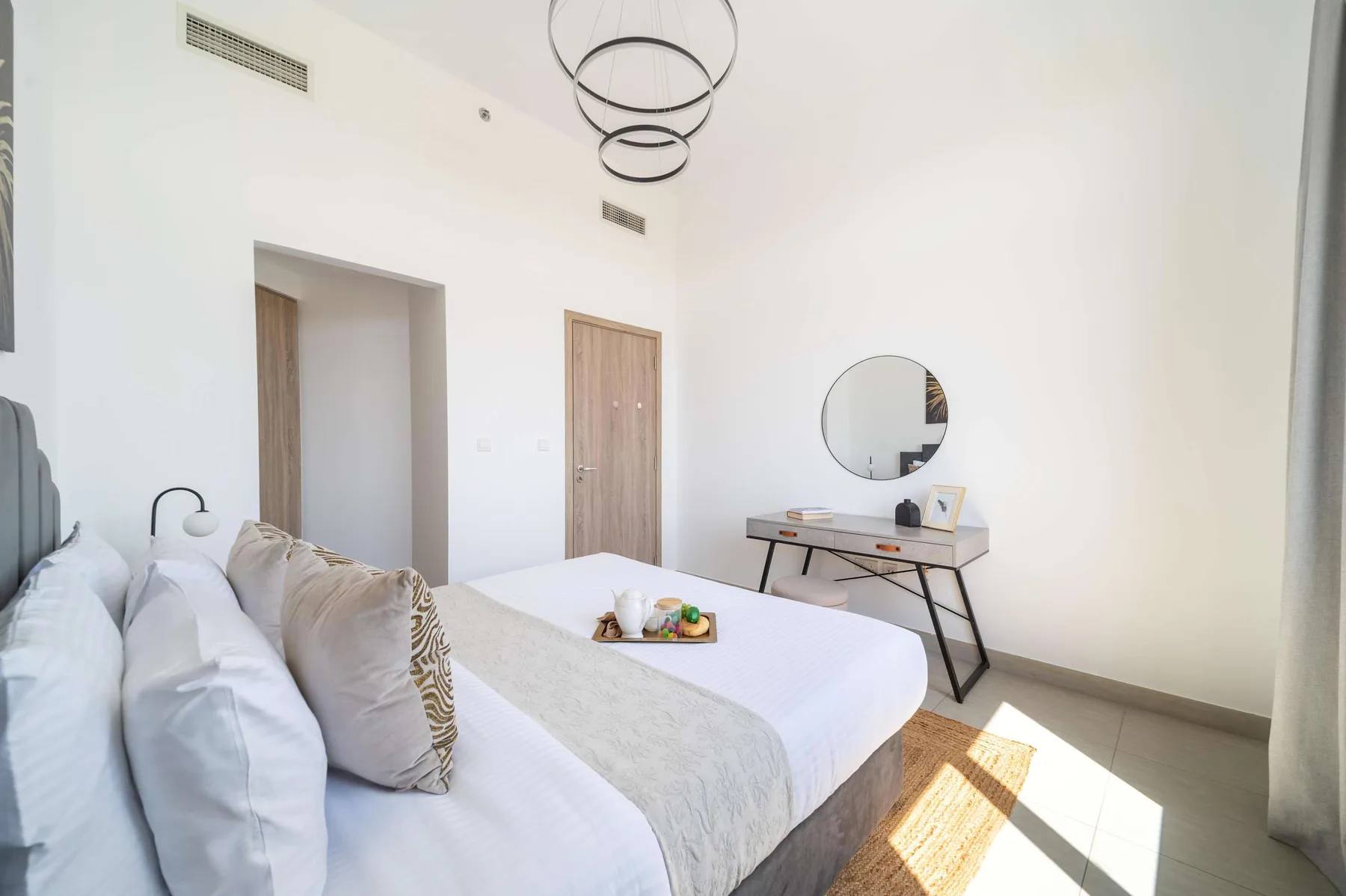 Un dormitorio luminoso con una cama y un escritorio bajo un espejo redondo.
