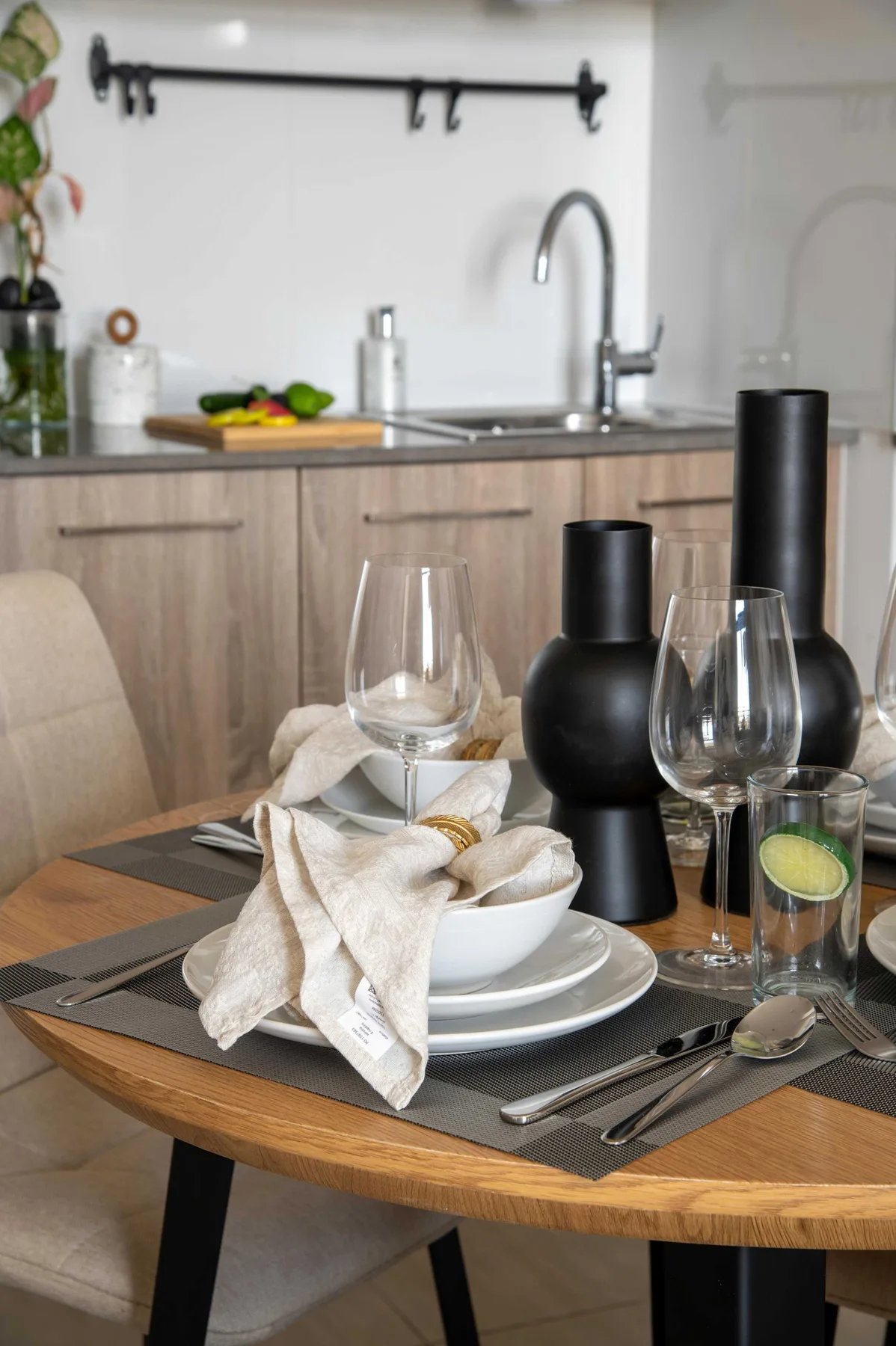 Una mesa de comedor está puesta con platos, copas, servilletas y jarrones decorativos oscuros.