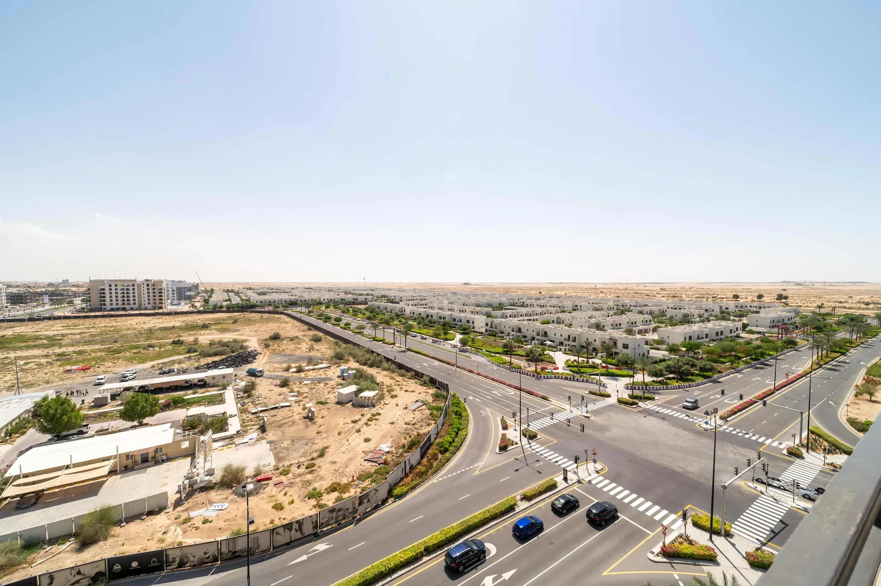 Una amplia intersección urbana con pasos peatonales y edificios bajos bajo un cielo despejado.