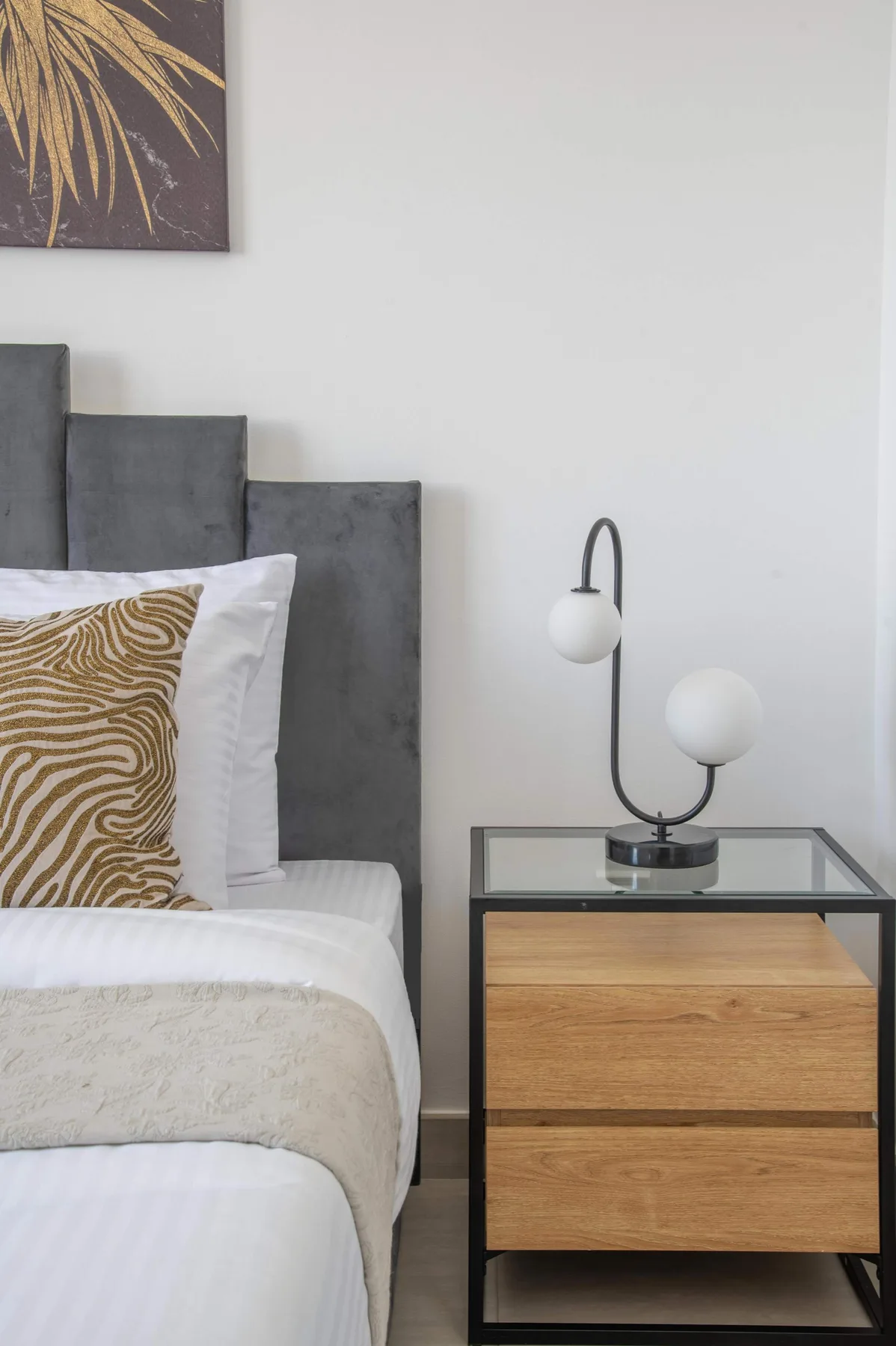 Un dormitorio con una cama junto a una mesita de madera y una lámpara moderna.