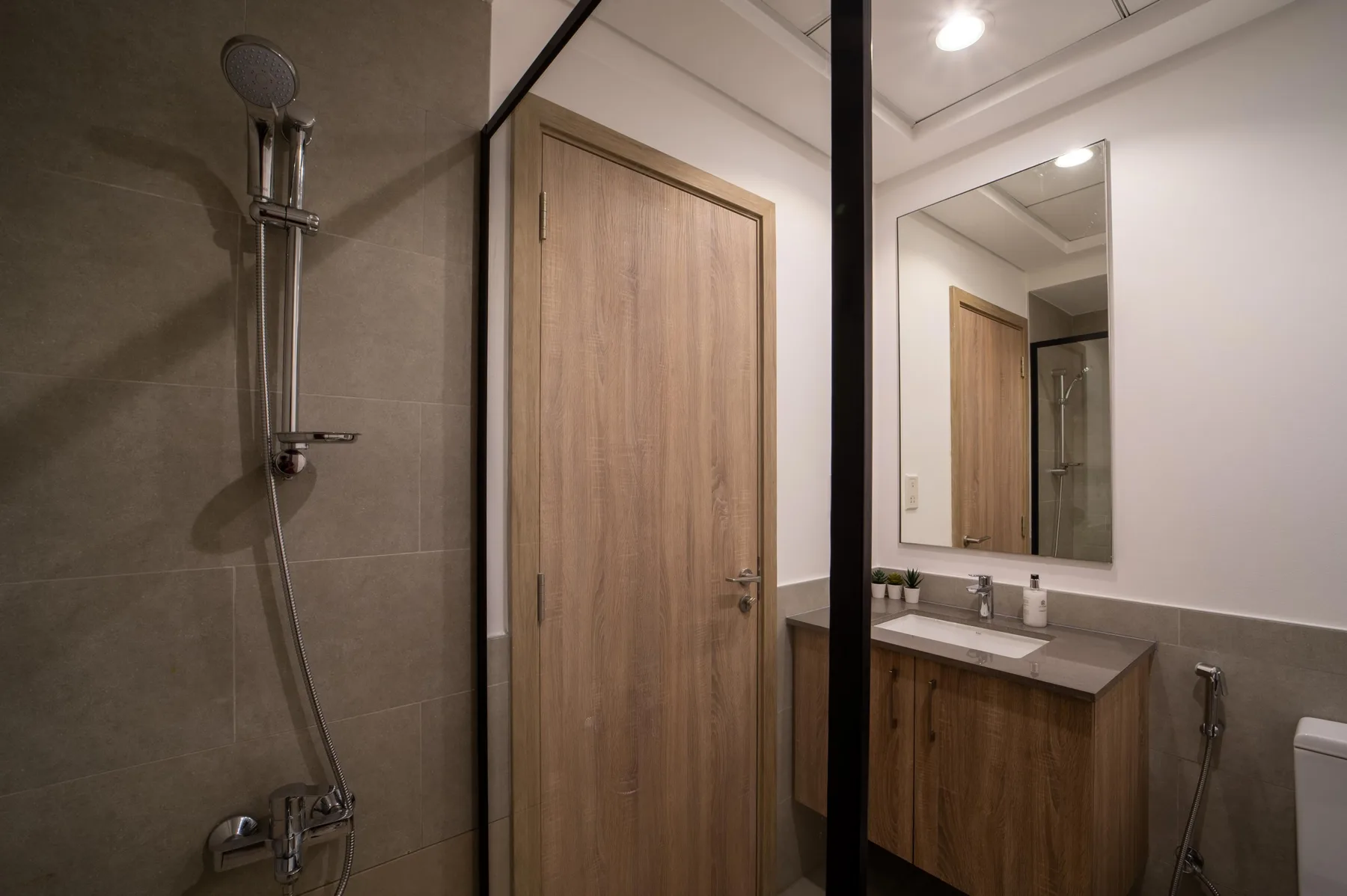 Un baño con mampara de ducha, puerta de madera y lavabo con mueble.