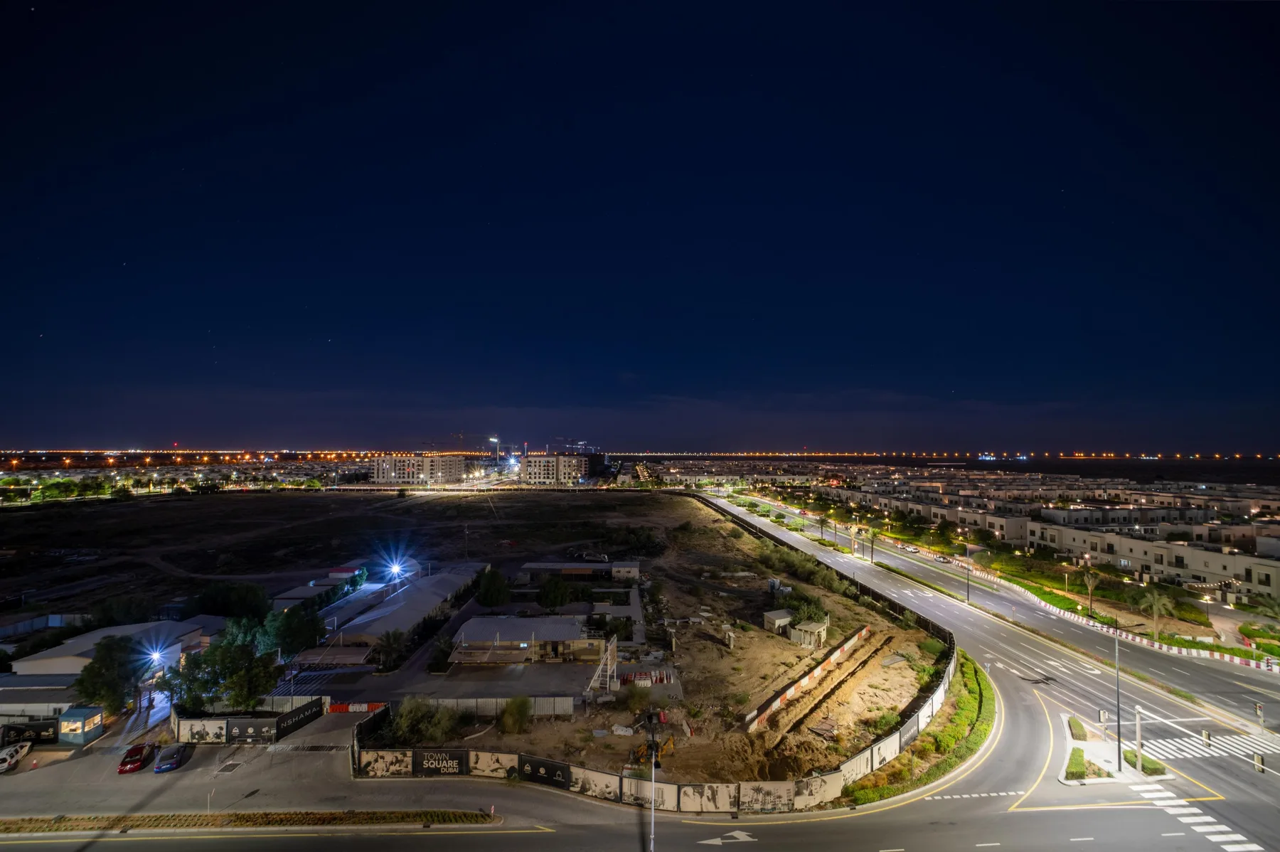 Un paisaje urbano nocturno muestra una carretera iluminada y edificios cercanos.