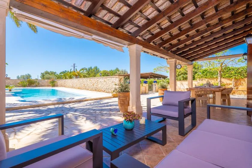 A shaded patio with lounge seating overlooks a swimming pool and garden.