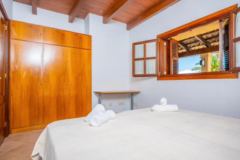 A bedroom with a white bed, wooden wardrobe, and open window.
