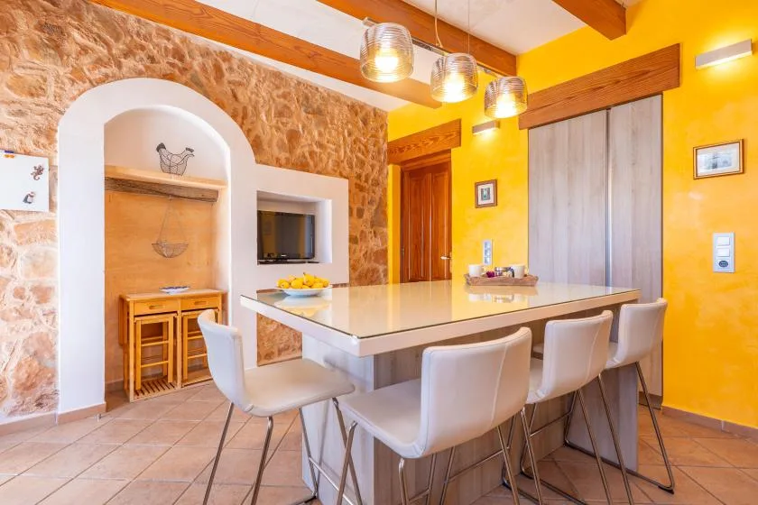 A bright dining area with a long table, white seating, and warm yellow walls.