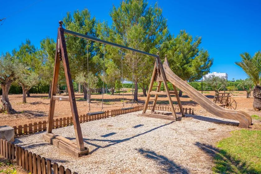 An outdoor playground with a wooden swing set and slide on a gravel surface.