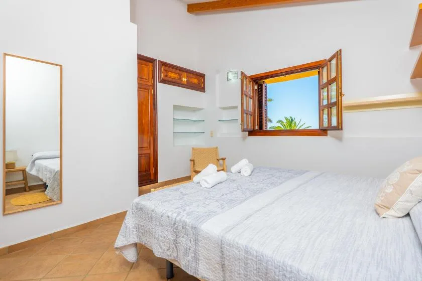 A bedroom with a bed, an open window, and a mirror on the wall.