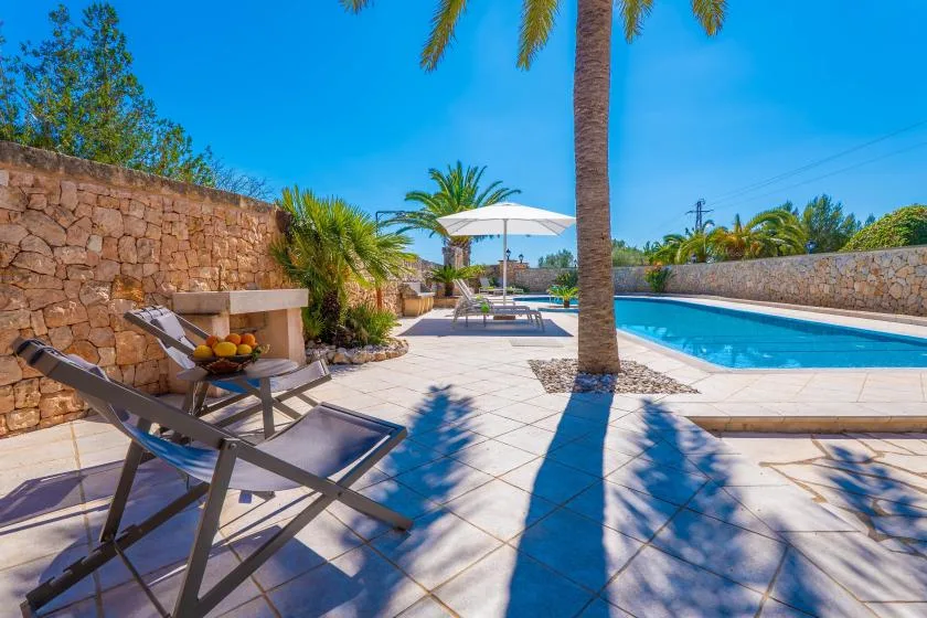 A sunlit poolside patio with lounge seating and a white umbrella.