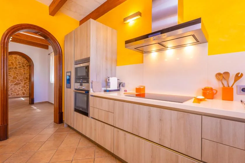 A modern kitchen with light wood cabinets, built-in appliances, and a bright yellow wall.