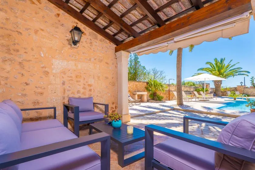 A shaded patio seating area overlooks a swimming pool and palm trees.
