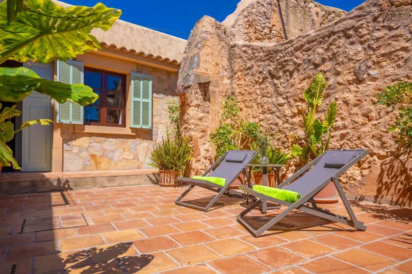 A sunny stone courtyard with two lounge chairs and leafy plants.