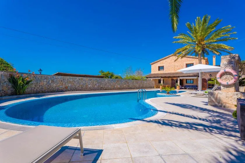An outdoor swimming pool sits beside a patio and a building under a clear blue sky.