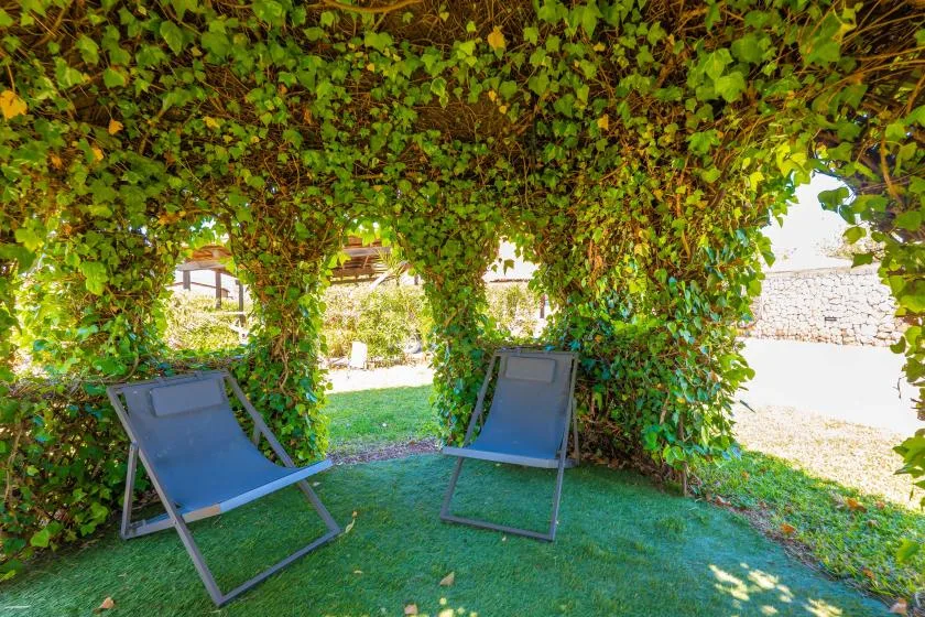 A leafy garden seating area with two reclining chairs beneath a vine-covered canopy.