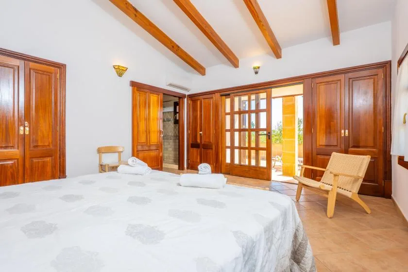 A bedroom with a large bed and wooden doors opening onto a patio.