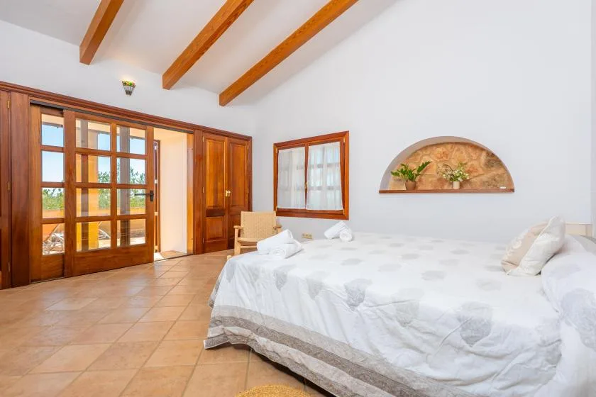 A bright bedroom with a large bed and wooden doors opening onto a balcony.