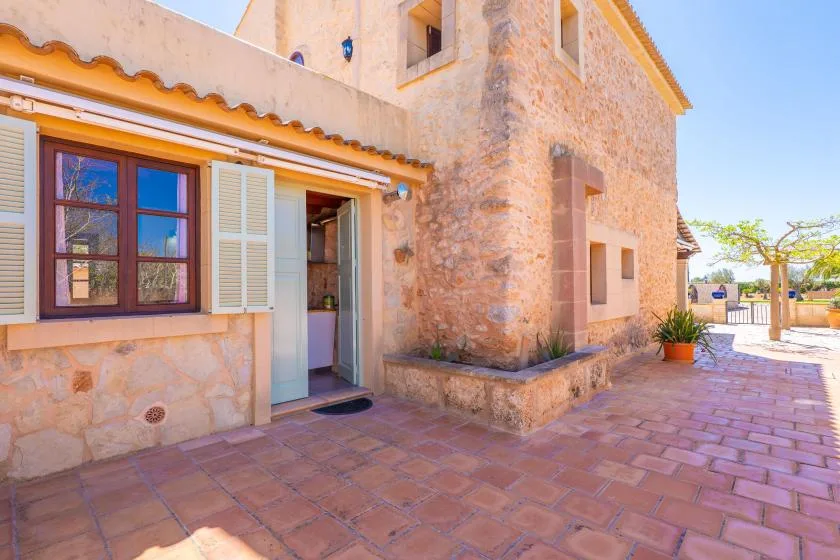 A stone house entrance opens onto a paved courtyard with a potted plant.