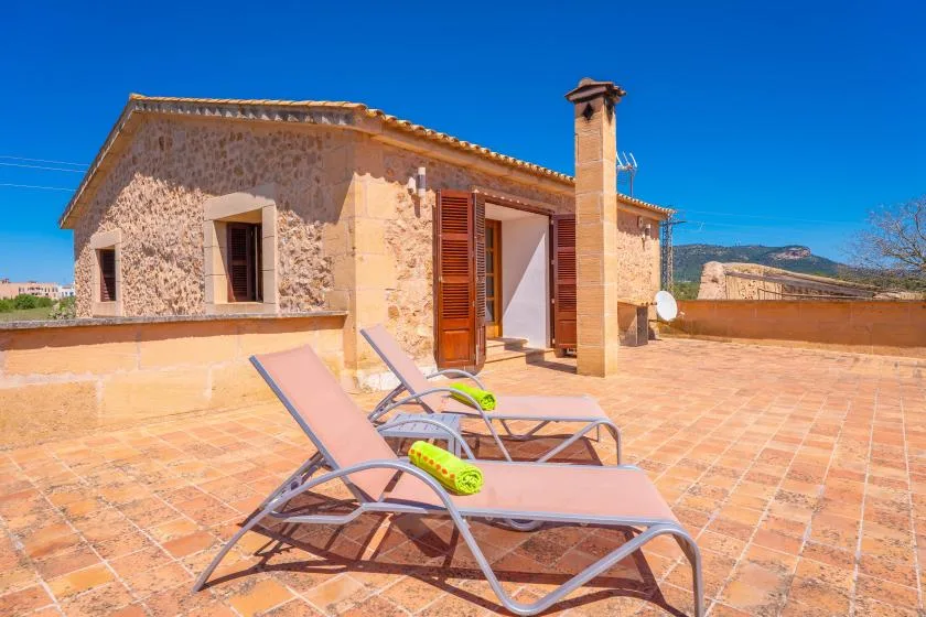 A sunny rooftop terrace with reclining loungers beside a rustic stone building.