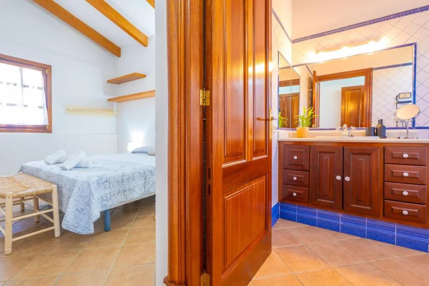 A bedroom with a bed and a bathroom vanity visible through an open wooden door.