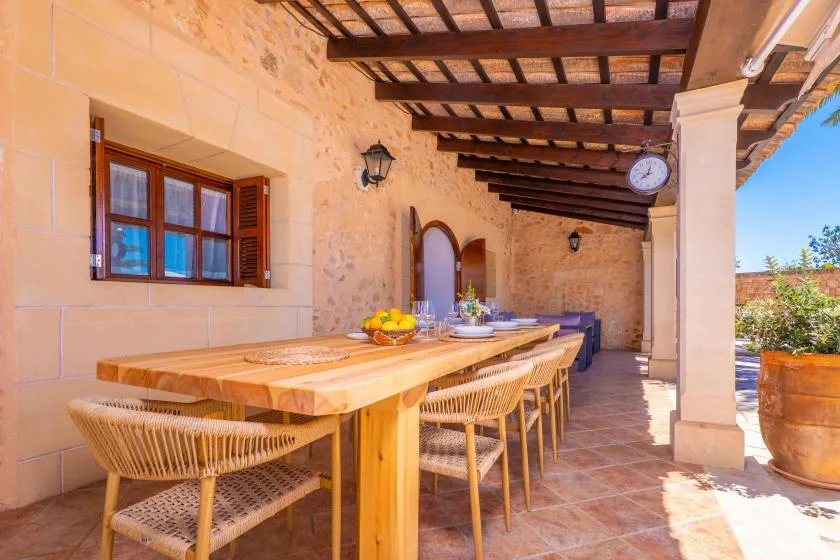 A covered outdoor dining area with a long table and woven seating.