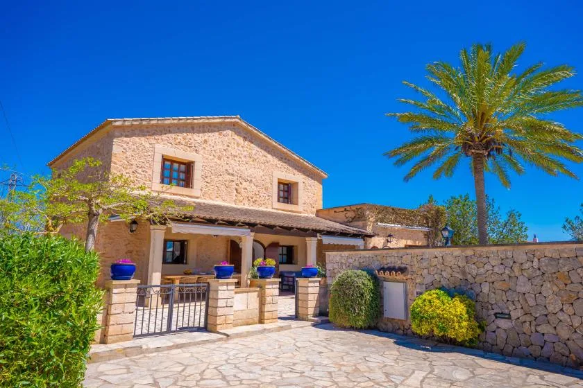 A stone building with a paved courtyard, low wall, and palm tree.