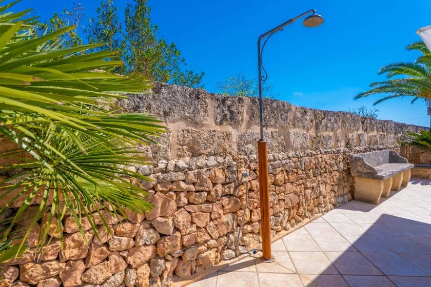 A tiled outdoor patio beside a stone wall, with a bench and leafy plants.