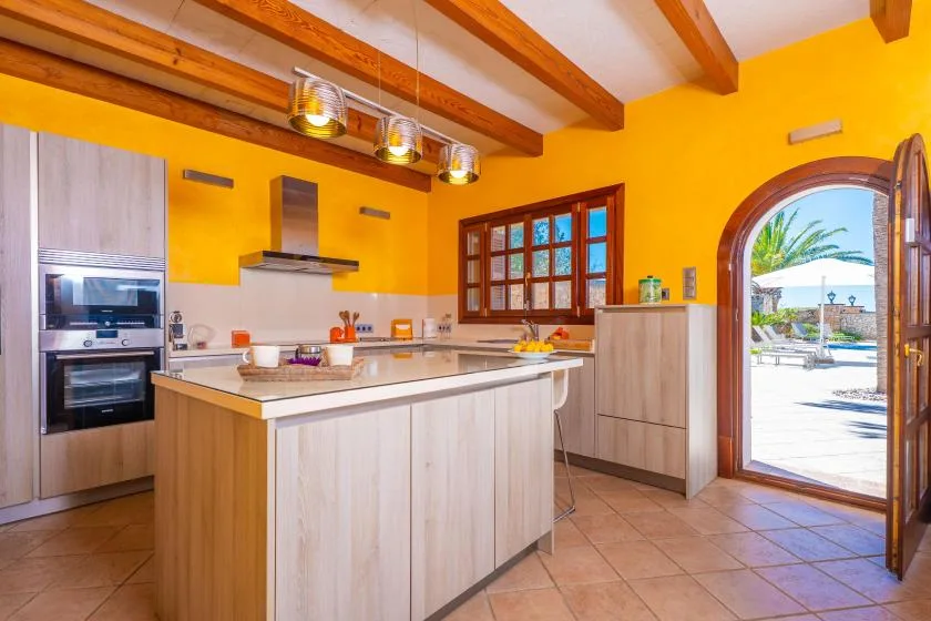 A bright kitchen with a central island, wooden cabinetry, and an arched doorway.