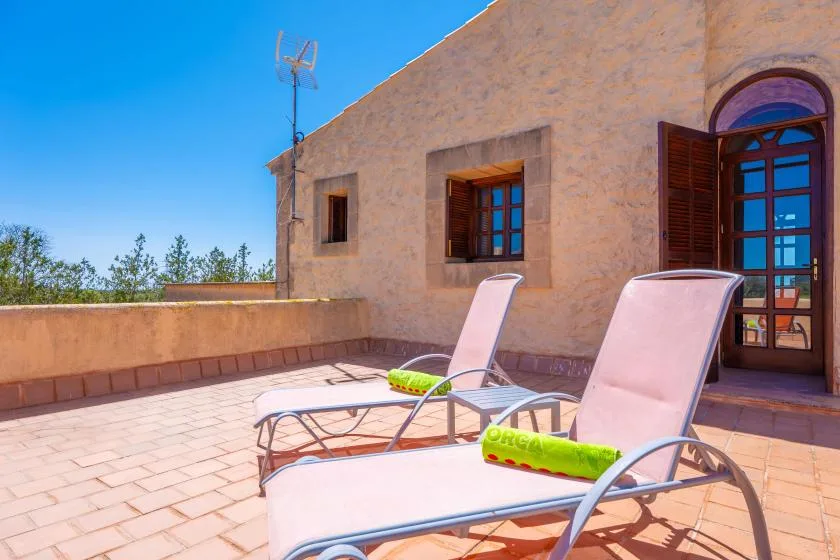 A sunlit rooftop terrace with reclining seating beside a stone exterior wall.