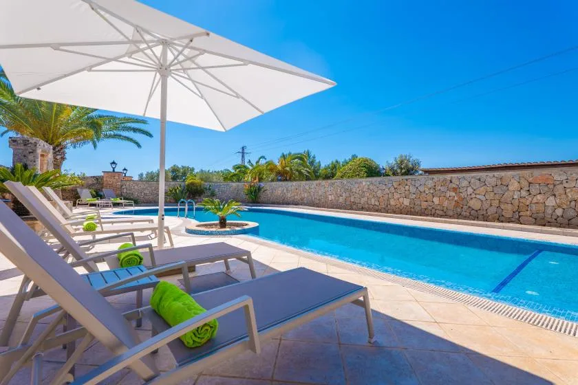 An outdoor swimming pool beside sun loungers and a large white umbrella.