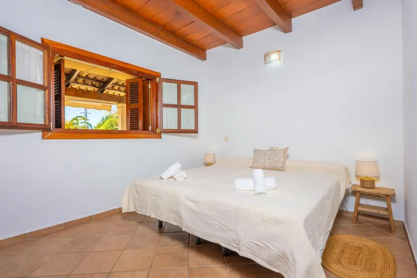 A bedroom with a bed beneath a wooden-beam ceiling and an open window.