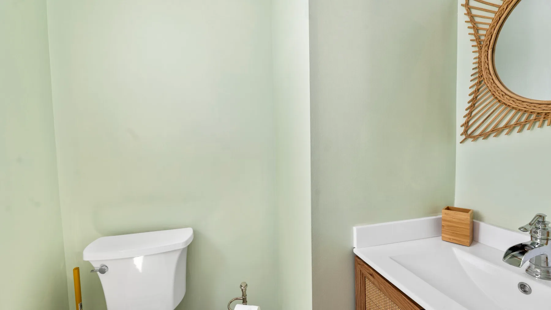 A bathroom with a toilet, sink, and round mirror.