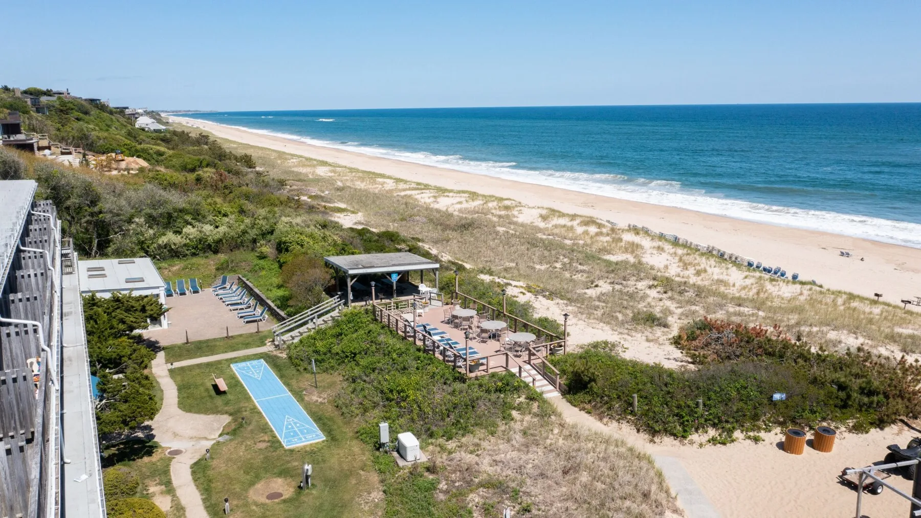 A coastal beach and ocean extend beside landscaped grounds and an outdoor seating area.