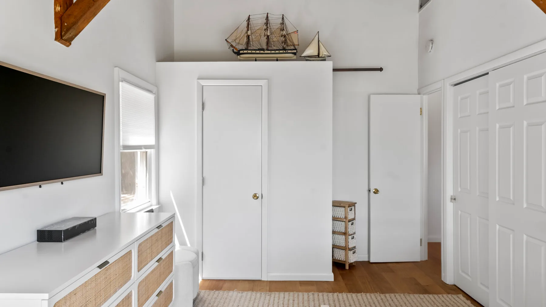 A bright bedroom with a wall-mounted television and white doors.
