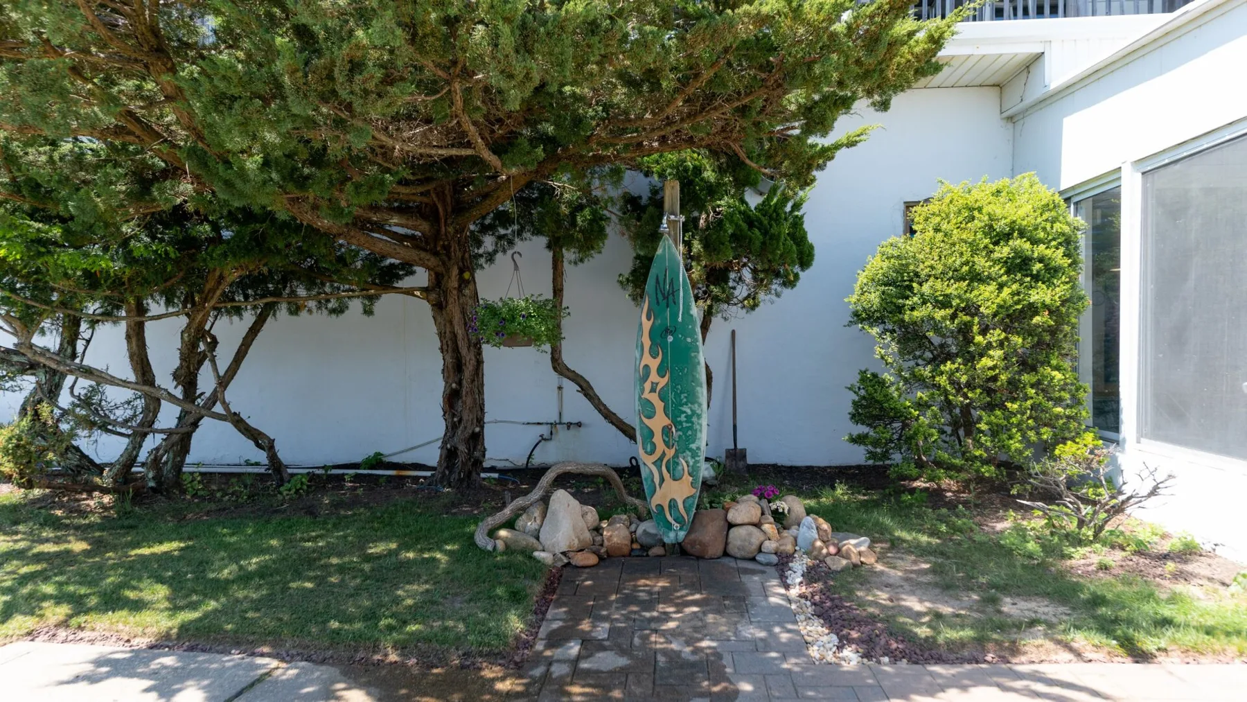 A small garden path leads to a decorative surfboard beneath trees.