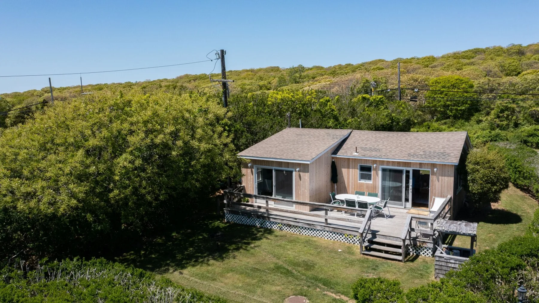 A small cabin surrounded by dense greenery, with a lawn and wooden deck.