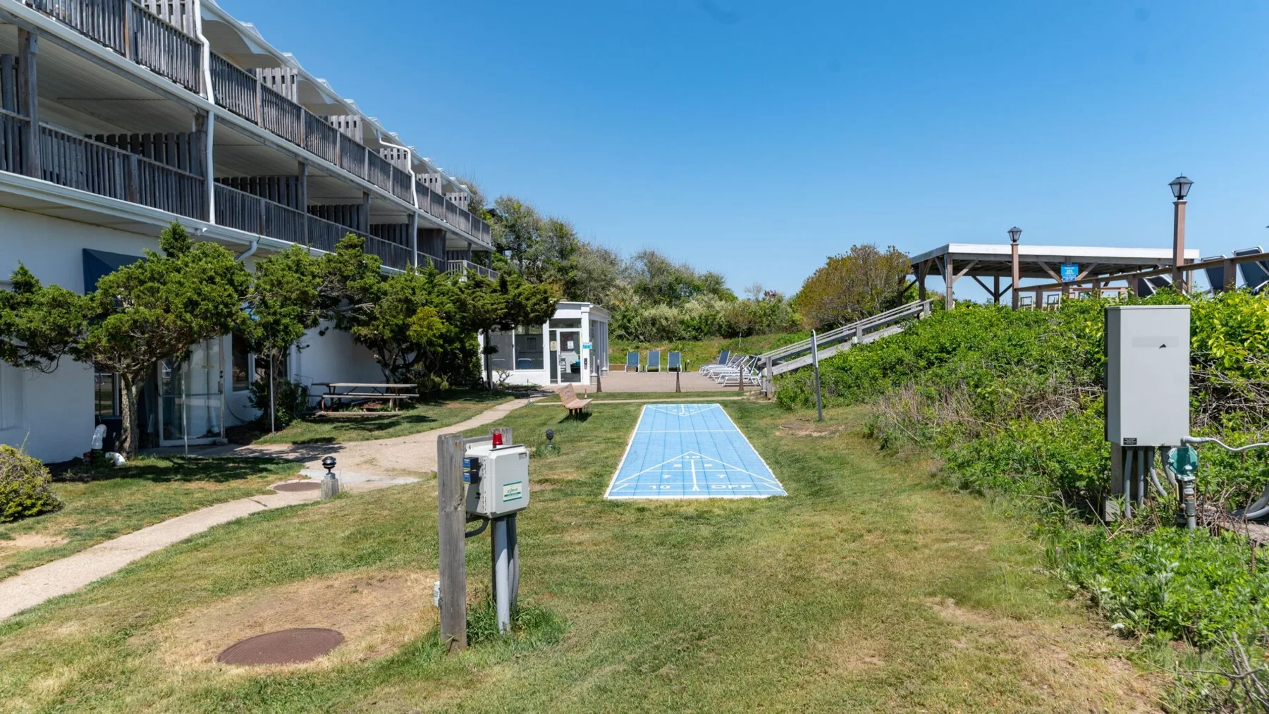 An outdoor recreation area has a blue court, grassy grounds, and nearby buildings.
