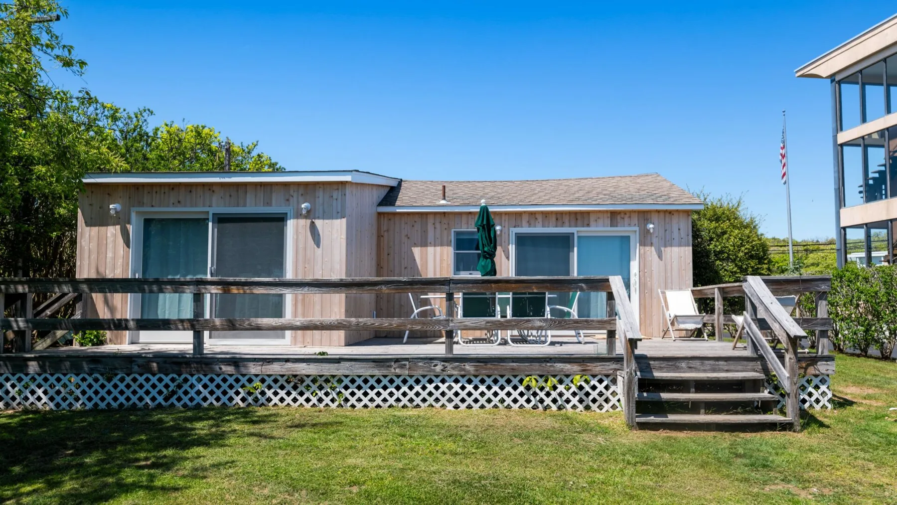 A low building stands behind a wooden deck and stairs in a grassy outdoor setting.