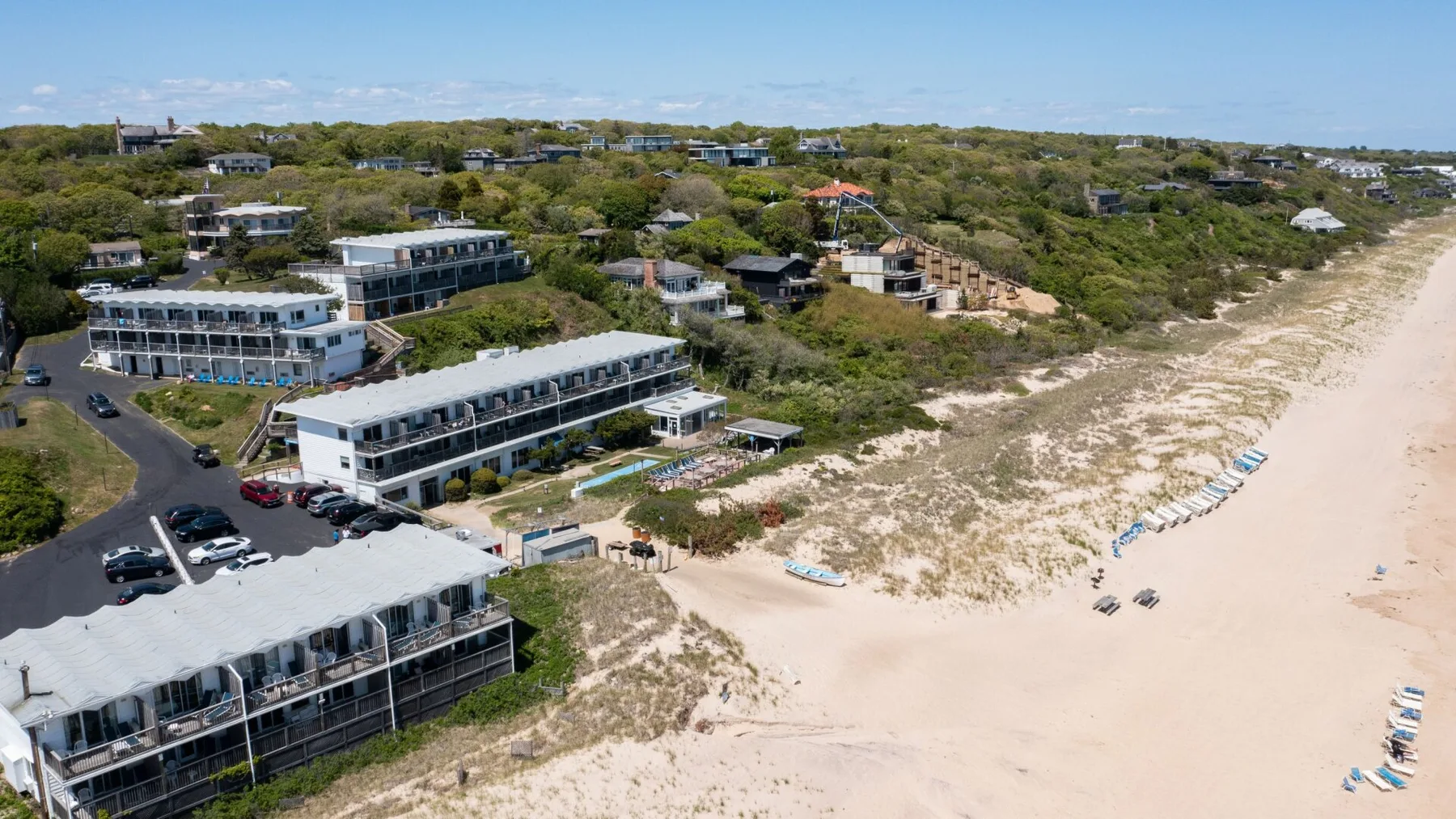 Aerial view of beachfront buildings beside a sandy beach and coastal vegetation.