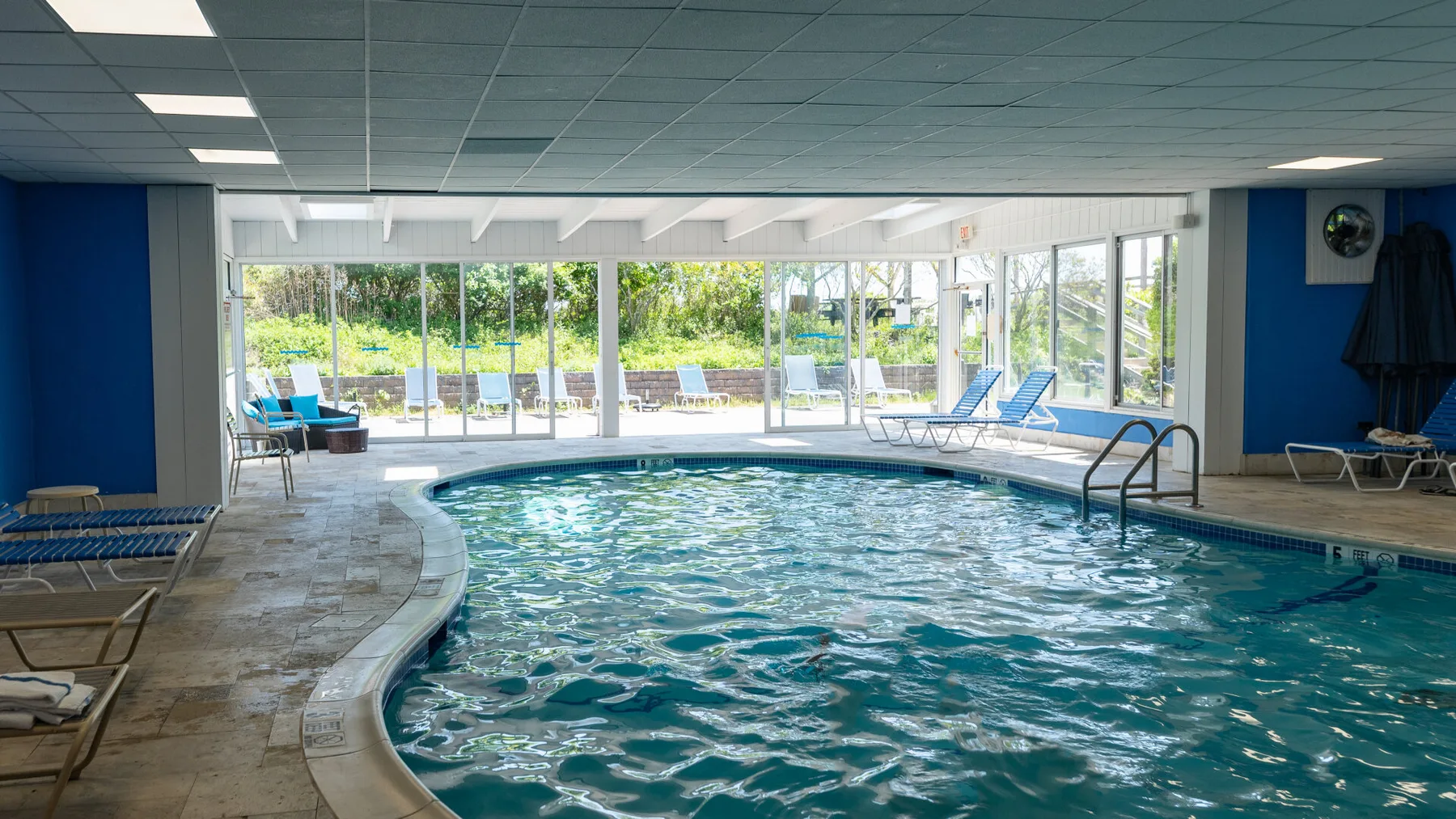 An indoor swimming pool with lounge seating beside large windows.