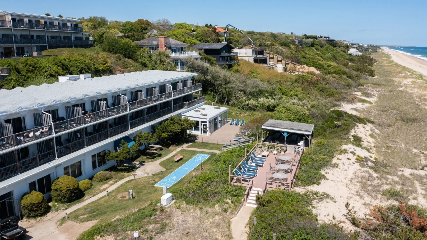 Aerial view of a coastal resort with buildings, a pool, and the beach.