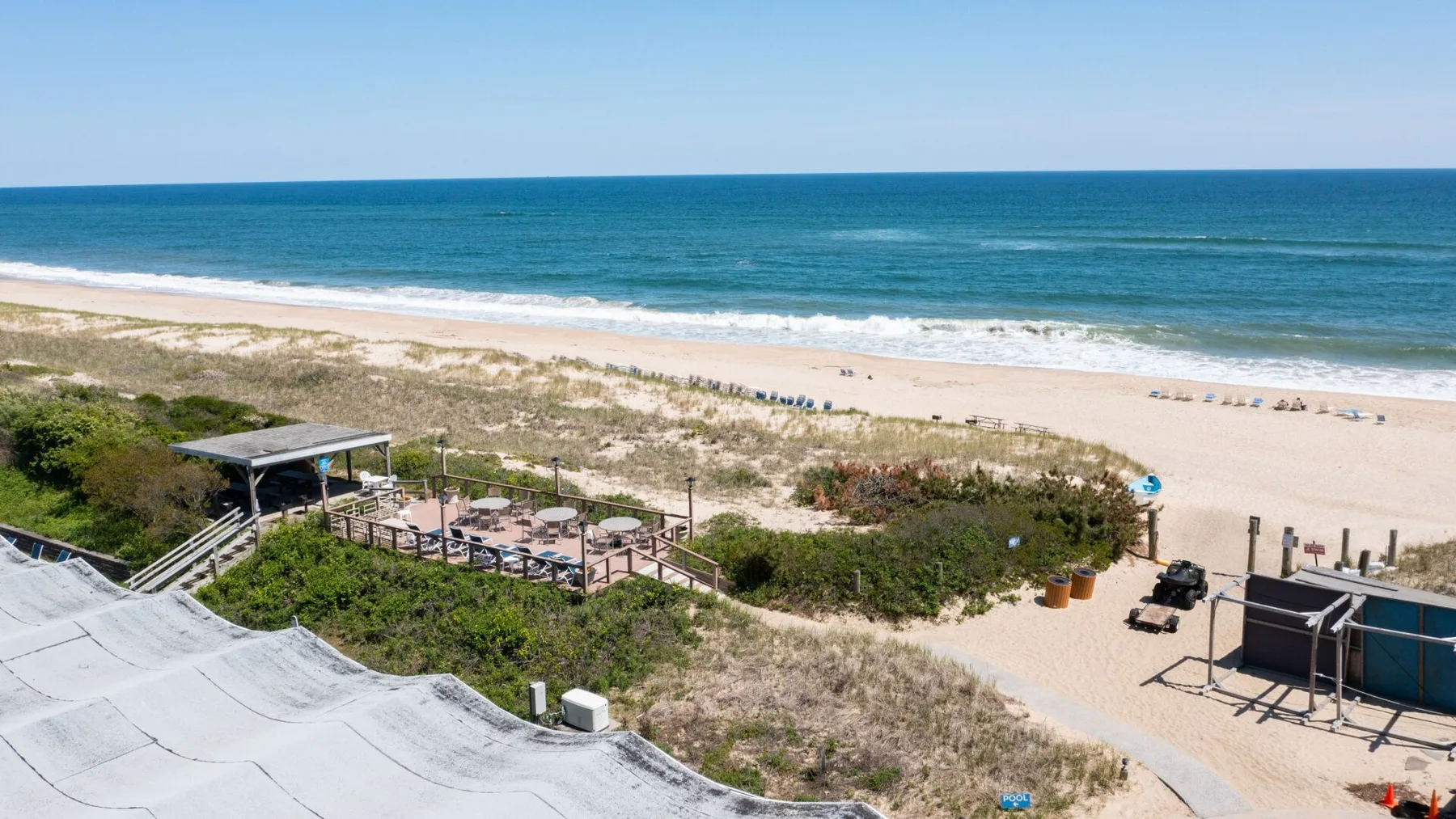A beach scene with ocean waves beyond sandy dunes and a beachside seating area.