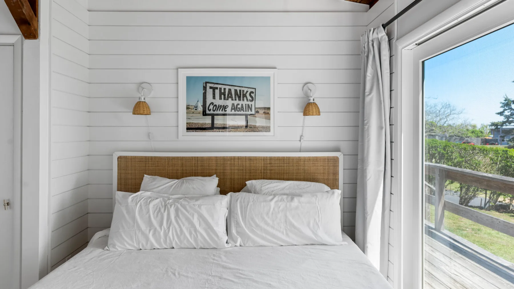 A bedroom with a bed beneath a framed sign and a large window.