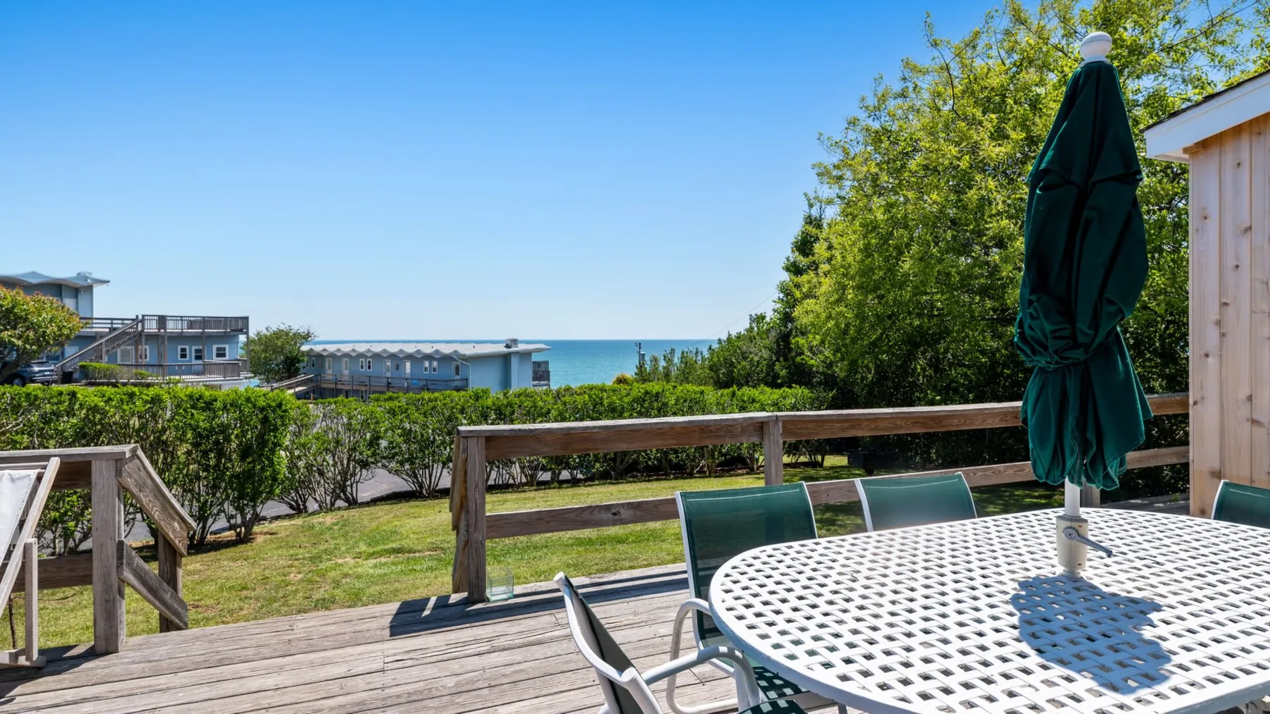 A wooden deck overlooks a grassy yard, with outdoor seating and the water beyond.