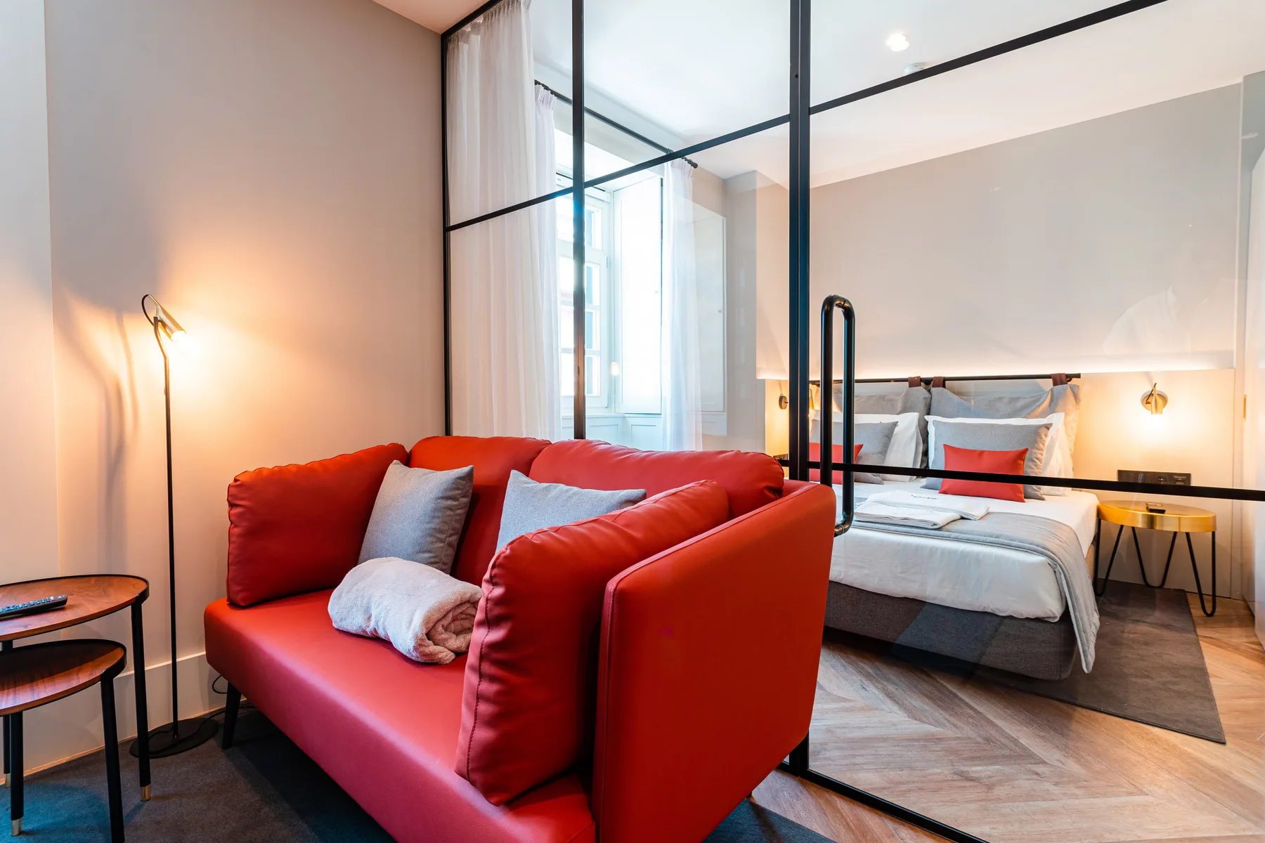 Un dormitorio y una zona de estar están separados por un tabique de vidrio, con asientos rojos delante.