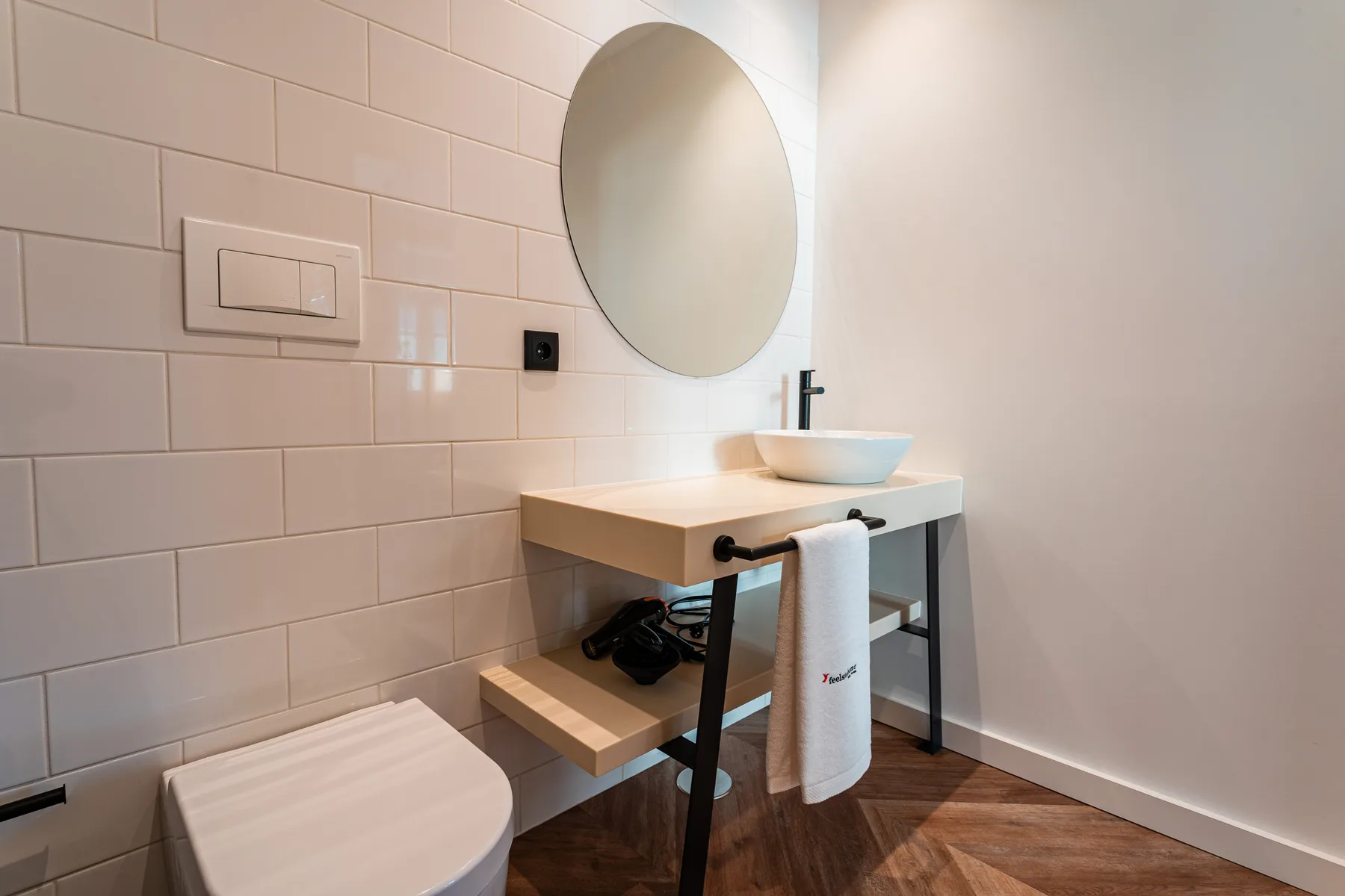 A bathroom with a vessel sink, round mirror, and tiled wall.