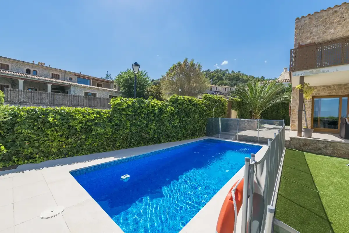 An outdoor swimming pool beside a building, with green hedges and a paved deck.