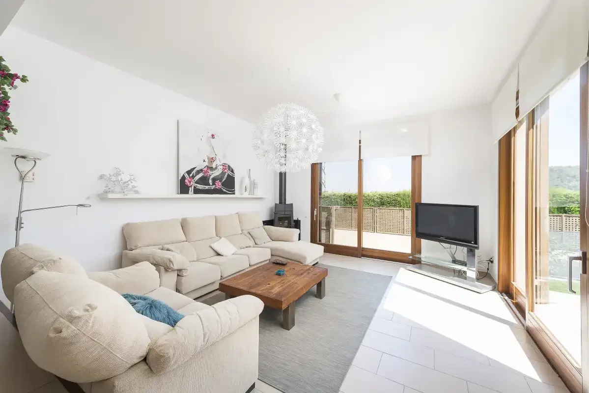 A bright living room with light seating, a wooden coffee table, and large glass doors.