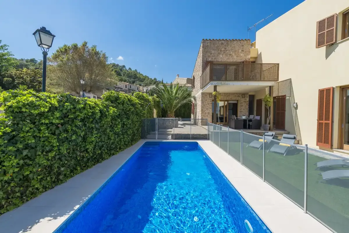 A narrow outdoor swimming pool beside a house and glass patio railing.